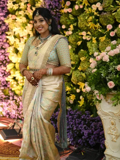 A full-length view of the bride in her pastel green and off-white Kanchivaram ensemble, standing against a beautiful floral backdrop.