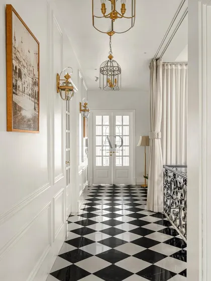 A hallway designed with careful planning and craftsmanship. The classic black and white diamond-patterned floor provides a bold graphic foundation, complemented by white paneled walls and ornate, cage-style pendant lights for a touch of Parisian flair.