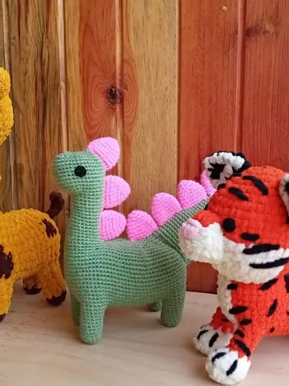 A trio of colorful animal friends: a yellow giraffe, a green dinosaur with pink plates, and a bright orange tiger.