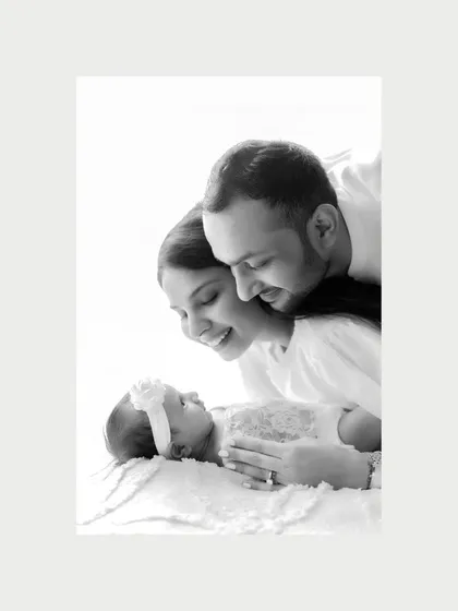 In a tender black and white close-up, new parents gaze down at their sleeping newborn with overwhelming love. This photograph captures the profound, silent conversation of a family just beginning, a moment of pure wonder and gratitude.