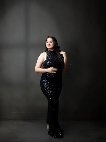 A chic and sophisticated maternity portrait. The expectant mother wears a sparkling black sequin gown, captured in a moment of serene contemplation.