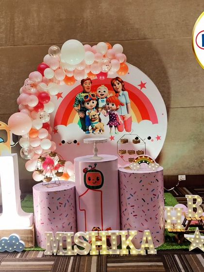 A pretty-in-pink Cocomelon-themed first birthday. This setup features a pink balloon arch, character cutouts, and a 'MISHIKA' marquee.