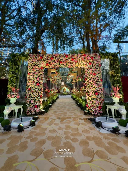 A grand floral entrance arch for an outdoor wedding, made with a profusion of pink and red flowers, leading to a magical walkway.