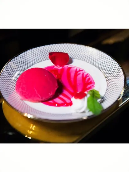 A vibrant raspberry dessert, beautifully plated with a bright pink glaze and delicate garnishes. It's almost too pretty to eat.