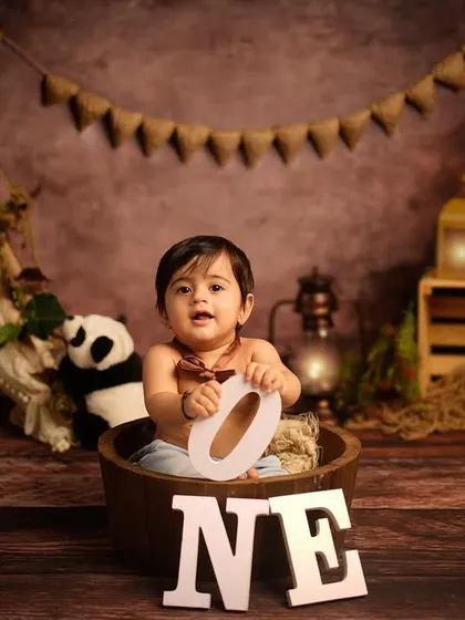 A happy boy in a tub, ready for his first birthday photos. The rustic, jungle-themed backdrop with stuffed animals creates a playful atmosphere for his milestone session.