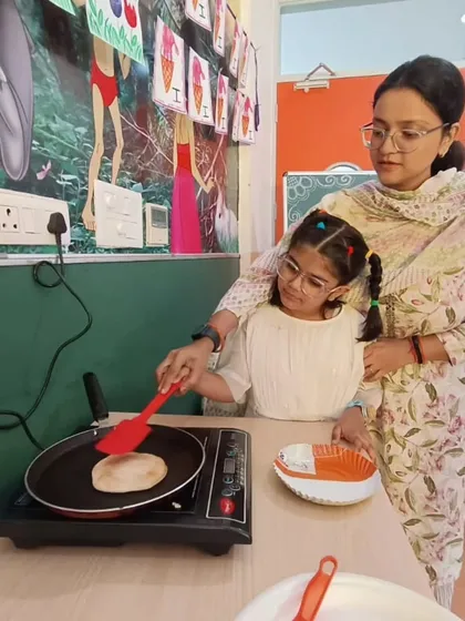 A teacher guides a student as she learns to flip a pancake on an induction cooktop. Our culinary arts program emphasizes hands-on learning and safety in the kitchen.