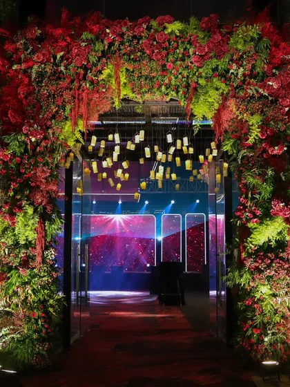 A grand floral archway, bursting with red blooms and lush greenery, creates a stunning transition into the main event space, hinting at the opulence within.