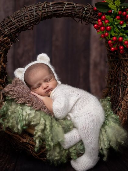 A close-up of the baby in the winter wreath, focusing on the peaceful sleeping face and the cozy bear hat.