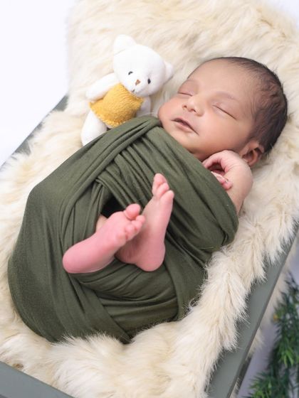 A newborn rests on a soft fur blanket, swaddled in an olive green wrap. We focus on capturing those tiny feet and peaceful expressions that you'll want to cherish.