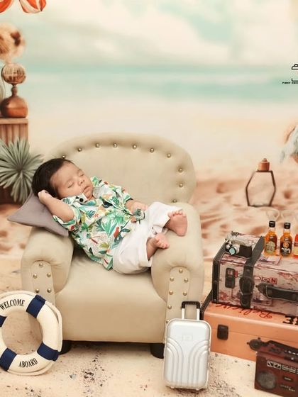 A full view of the 'Tiny Traveler' vacation set. This wide shot shows the entire creative setup, from the sandy floor to the ocean backdrop, with the sleeping baby as the star.