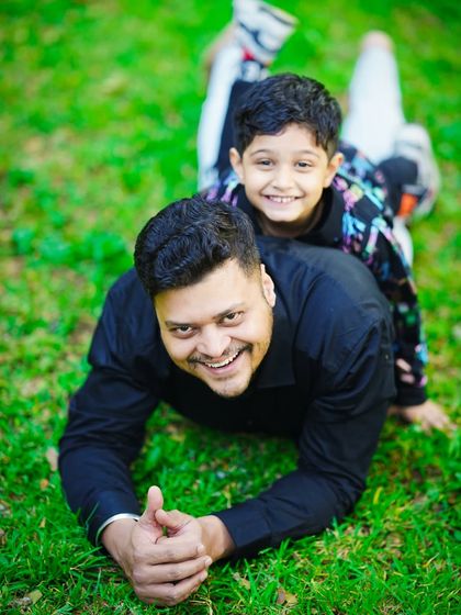 A fun and playful moment between father and son, laughing together while lying on the grass in the park.