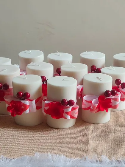 A set of classic white pillar candles decorated with red and white striped ribbons and festive berry details, perfect for simple and elegant holiday decor.