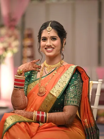 A classic portrait of a Maharashtrian bride. Her makeup is subtle and enhances her natural features, paired with a traditional orange and green saree and a simple bindi.