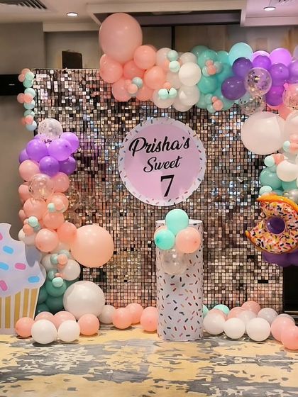 A sweet candy-themed birthday setup with a silver shimmer wall, pastel balloons, and large cupcake and donut props.