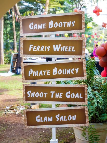 A rustic wooden signpost for a pirate-themed party, pointing towards the 'Ferris Wheel', 'Pirate Bouncy', and 'Glam Salon'.