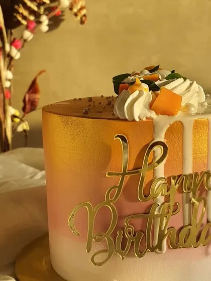 Another angle of this stunning mango birthday cake, showing the smooth ombre frosting and the elegant gold 'Happy Birthday' topper.