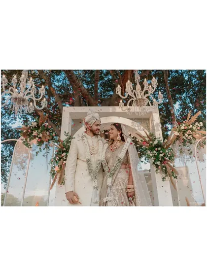 A beautiful portrait of the couple standing before their elegant beachside mandap. The chandeliers and floral arrangements create a luxurious and romantic setting.