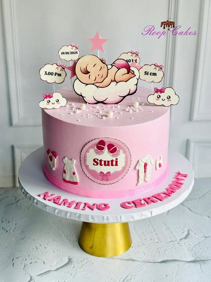 A beautiful cake for baby Stuti's naming ceremony. This pink cake is decorated with baby clothes, birth details, and a sweet sleeping baby topper.