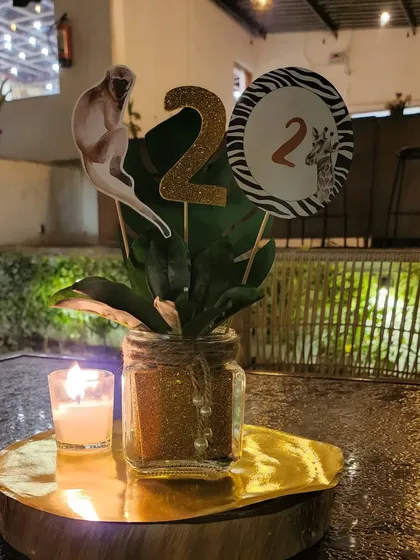 A jungle-themed table centerpiece for a second birthday party. The arrangement includes a glittery number '2', an animal cutout, and a candle on a rustic wood slice, perfect for adding themed touches to each table.