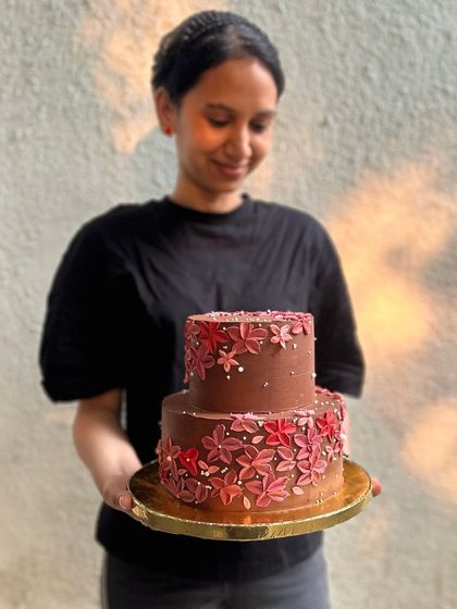 Our baker, Sanjana, proudly holding a finished two-tiered chocolate wedding cake. So much love and care from our team goes into every single creation before it reaches your celebration.