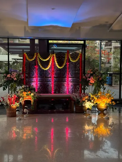 A traditional seating area for a Mehendi ceremony, featuring a carved wooden screen, marigold garlands, and brass pots filled with flowers, all beautifully lit for an evening event.