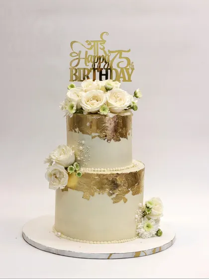 A two-tier cake for a 75th birthday, but with the elegance of a wedding cake, featuring white roses and gold leaf.