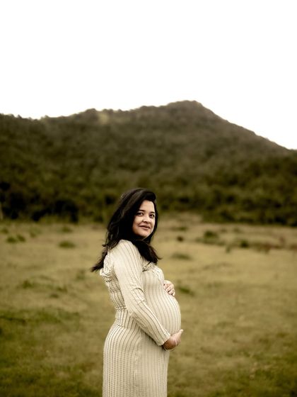 A classic and beautiful solo maternity portrait. The mom-to-be stands in a field, cradling her bump and looking at the camera with a calm, confident smile.