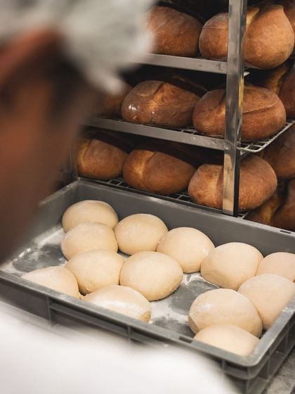 A rack full of freshly baked sourdough loaves next to trays of dough balls ready for service. This is the engine room of our bakery.