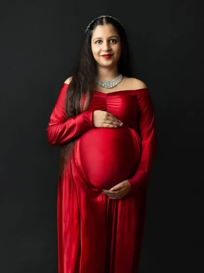 A classic and direct portrait of a radiant mother-to-be in a striking red gown against a solid black background. This simple setup puts all the focus on her joyful expression and beautiful baby bump.