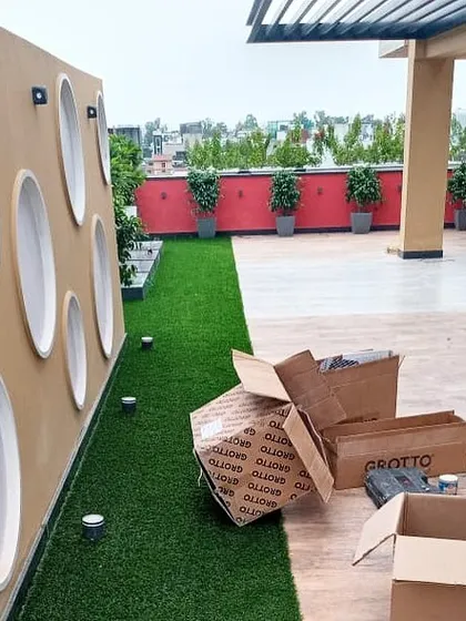 A work-in-progress shot of a terrace installation. This view shows the newly laid artificial turf and the placement of ground-level spotlights along a decorative wall, highlighting the steps involved in the process.