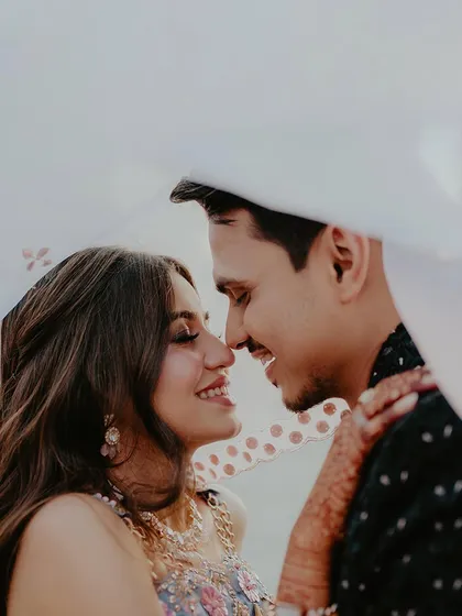 A joyful close-up of a couple smiling at each other from under a sheer dupatta. This candid moment is full of laughter and intimacy, perfect for capturing authentic pre-wedding memories.