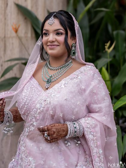 A beautiful medium shot of a bride in her pastel pink lehenga, showcasing her layered necklace and gentle smile.