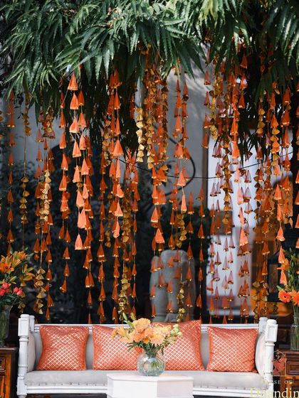 A stunning backdrop of hanging floral tassels in shades of orange, creating a beautiful photo opportunity and adding texture and movement to the couple's seating area.