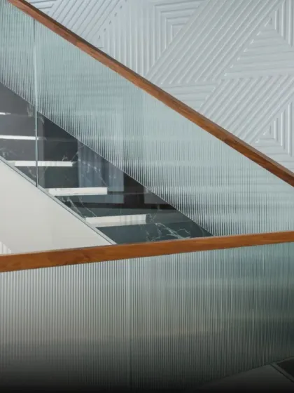 Details of a staircase with a textured geometric wall panel. The design creates a dynamic interplay between the clean lines of the glass railing and the intricate pattern on the wall.