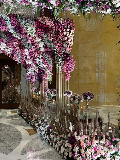 Take a walk down this gorgeous entrance, festooned with florals in a burst of purple hues. The modern golden pillars and dramatic floral arch create a grand first impression. 💜