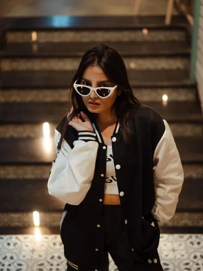 A cool and confident portrait of a model on illuminated stairs. The modern setting and her varsity jacket create a trendy, urban vibe.