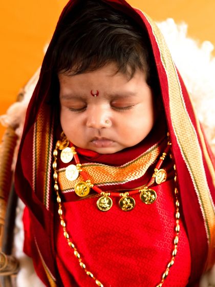 A detailed portrait of a baby girl in a traditional red outfit with gold coin necklaces, capturing the essence of Maharashtrian culture.