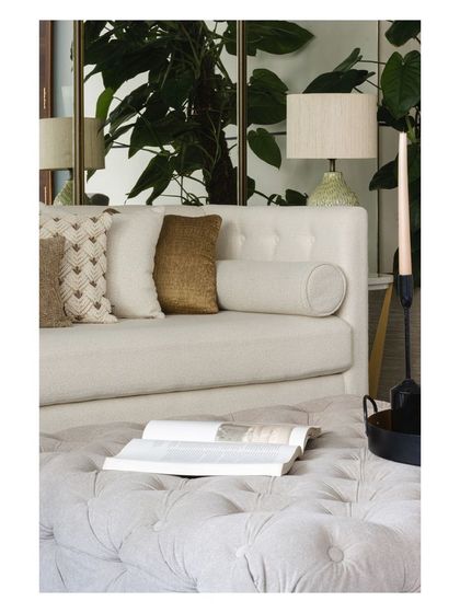 The interplay of textures, colors, and light. A tufted ottoman, a smooth sofa, and the reflection of a plant in a mirror create a rich and balanced composition.