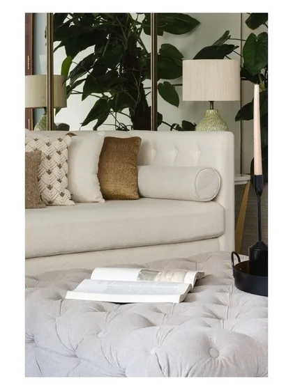 The interplay of textures, colors, and light. A tufted ottoman, a smooth sofa, and the reflection of a plant in a mirror create a rich and balanced composition.