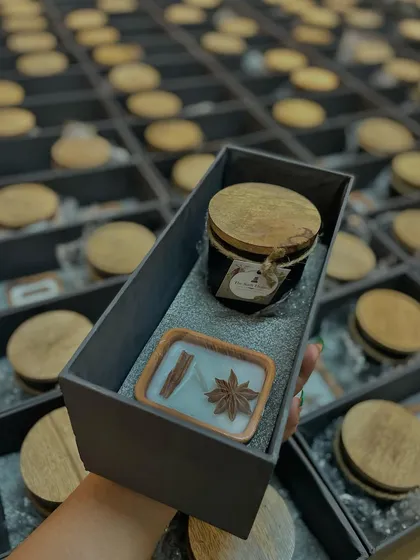A closer look inside one of our corporate gift hampers. This set includes a black jar candle with a wooden lid and a spice-topped candle in a wooden tray, all neatly arranged in a custom-fit box.