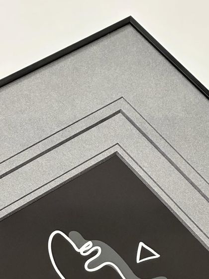 We love playing with mats to enhance an artwork. Here, we used double black-core grey mats with a V-groove and a minimal metal frame. The layered mats create depth and draw the eye toward the central artwork.