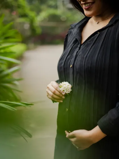 A close-up shot focusing on the baby bump, with the mother holding a small white flower. This artistic photo emphasizes the new life and delicate moments of pregnancy.