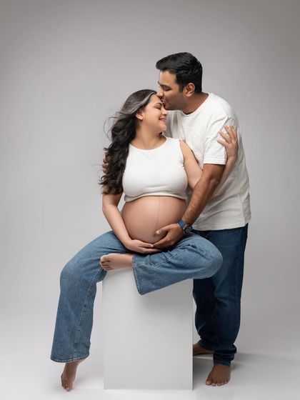 A tender forehead kiss. This casual setup with jeans and a white top feels relaxed, intimate, and authentic.
