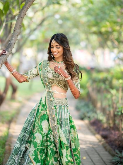 A modern bride glowing with timeless beauty. This look features soft, natural makeup and flowing curls, perfectly complementing her unique green printed lehenga.