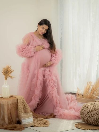 A full-length portrait of a mom-to-be looking radiant in a pink ruffled gown. The bright, airy feel of the lifestyle studio setup makes this photo feel so fresh and beautiful.