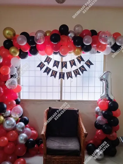 A red, black, and silver balloon arch setup in front of a window for a first birthday.
