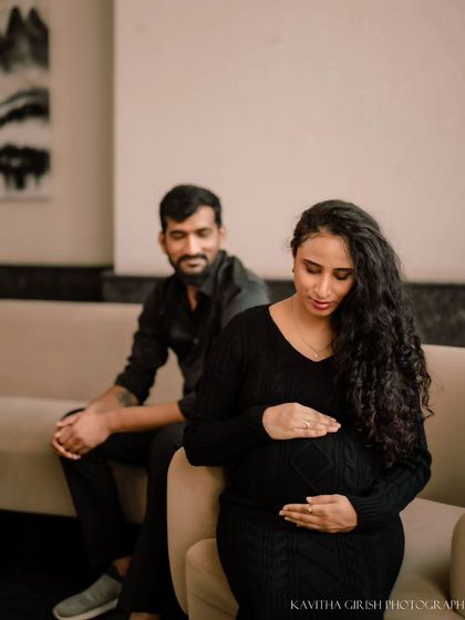 A quiet, reflective moment during an indoor maternity shoot. The woman looks down at her belly while her partner watches over her, creating a feeling of love and protection.
