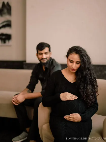 A quiet, reflective moment during an indoor maternity shoot. The woman looks down at her belly while her partner watches over her, creating a feeling of love and protection.