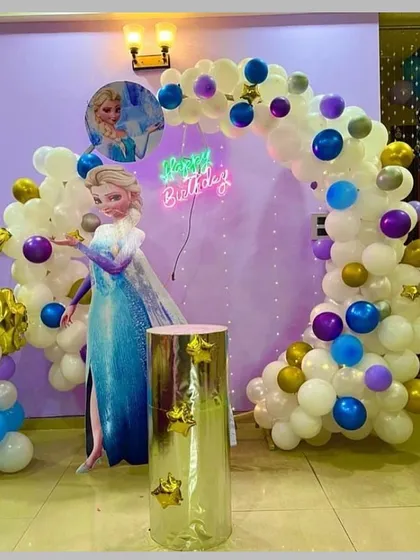 A 'Frozen' themed birthday party for a 4-year-old. The setup includes a beautiful balloon arch in icy whites and blues, with a large cutout of Queen Elsa and a themed pedestal.