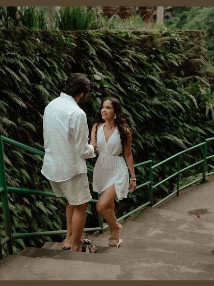 A sweet, interactive moment on a staircase surrounded by lush greenery in Bali. The groom leads the bride, and their shared glance is full of affection and happiness.